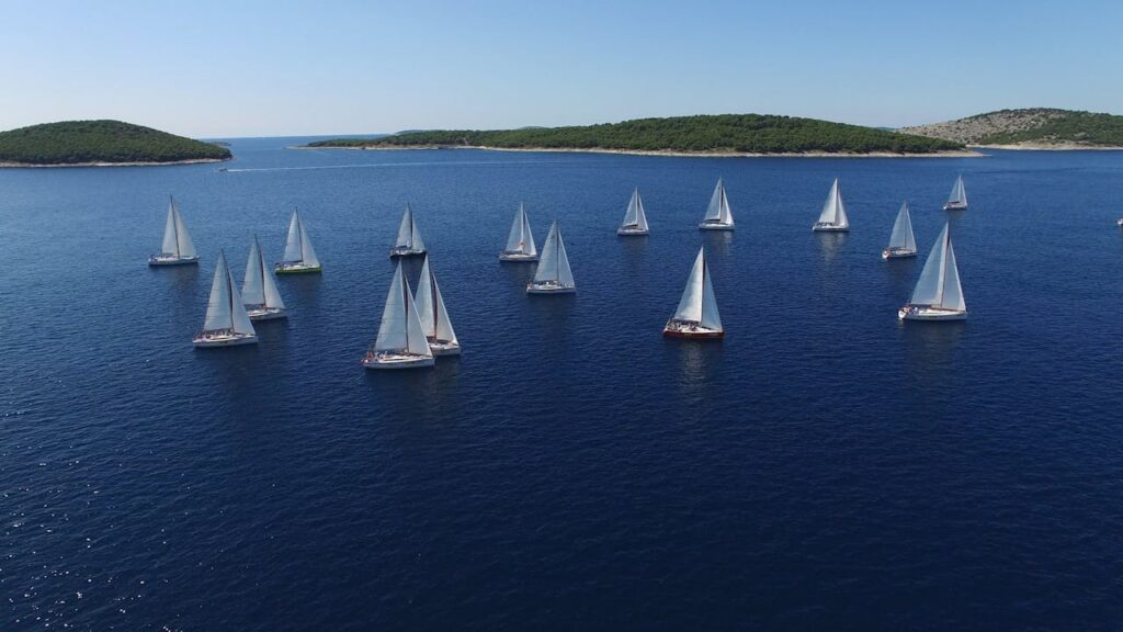 Sailboats racing in a summer regatta on a clear blue ocean surrounded by islands.